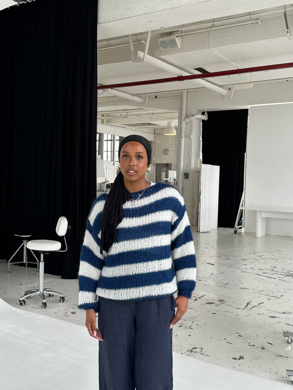 Pull oversize rayé bleu et blanc femme en tricot doux devant un mur blanc
